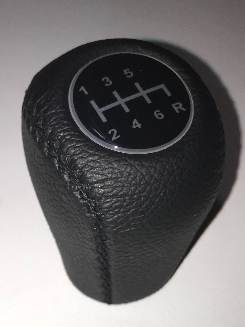 May include: Black leather gear shift knob with a silver and black gear pattern. The pattern shows the numbers 1, 2, 3, 4, 5, 6, and R.