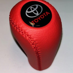 May include: Red leather gear shift knob with a black and silver Toyota logo.