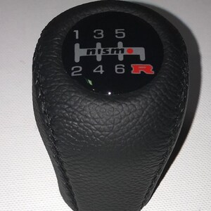 May include: Black leather gear shift knob with a silver and red Nismo logo and a 6-speed gear pattern.