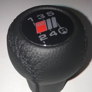 Könnte beinhalten: Schwarzer Lederschaltknauf mit einem schwarzen und grauen Schaltmuster und roten Akzenten. Die Zahlen 1, 2, 3, 4, 5 und R sind auf den Knauf gedruckt.