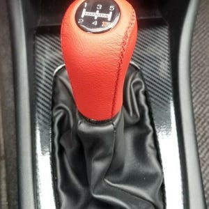May include: A red leather gear stick knob with a black shift boot. The knob has a black face with the Honda logo and gear shift pattern. The interior has a carbon fibre pattern.