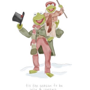 May include: An illustration of two green frogs dressed in winter attire. One frog holds a top hat and the other carries a cane. The text at the bottom reads "tis the season to be jolly & joyous."