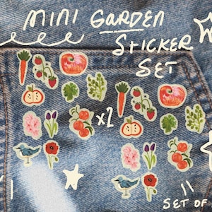 May include: A set of 22 mini garden stickers on a denim background. The stickers feature colorful illustrations of vegetables, fruits, flowers, and a bird. The text "MINI GARDEN STICKER SET" is written in white, along with star shapes.
