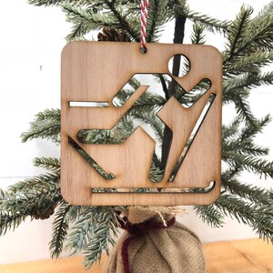 May include: Wooden Christmas ornament shaped like a skier, with a cutout design. The ornament is brown and has a red and white string attached.