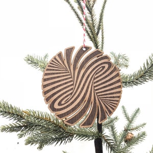 May include: A wooden Christmas ornament with a brown and black swirl pattern. The ornament is hanging from a red and white string on a green artificial Christmas tree.