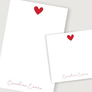 Puede incluir: Dos tarjetas blancas con corazones rojos y el nombre "Caroline Evans" escrito en cursiva roja.