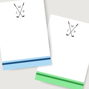 May include: Two white notepads with a blue and green stripe at the bottom. Each notepad has a black and white graphic of two crossed golf clubs with the letters "J", "W", and "P" in between.