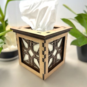 Puede incluir: Una caja de pa&ntilde;uelos de madera con un dise&ntilde;o geom&eacute;trico. La caja est&aacute; hecha de madera marr&oacute;n claro con detalles marrones oscuros. La caja de pa&ntilde;uelos es blanca y es parcialmente visible dentro de la tapa.