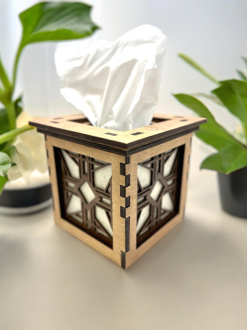 Puede incluir: Una caja de pa&ntilde;uelos de madera con un dise&ntilde;o geom&eacute;trico. La caja est&aacute; hecha de madera marr&oacute;n claro con detalles marrones oscuros. La caja de pa&ntilde;uelos es blanca y es parcialmente visible dentro de la tapa.