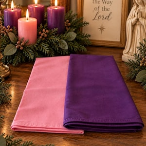 May include: Two folded fabric napkins, one in a solid light pink and one in a solid deep purple, are placed side by side. The napkins have a smooth, matte texture and clean, stitched edges, presenting a simple and functional design.