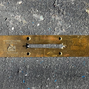 May include: A brass level with the inscription "Lambert Mulliken 1874 Pole Boston Mass". The level has a slot for a spirit level and several holes for screws.