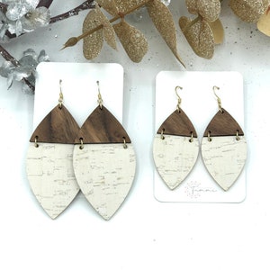 May include: A pair of brown and white cork and wood earrings with gold hooks. The earrings are shaped like a teardrop and have a white cork top and a brown wood bottom.