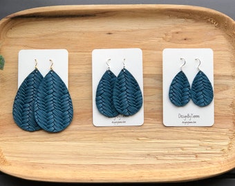 May include: Three pairs of teal blue leather earrings with a woven design. The earrings are displayed on white cards with the text "DesignByTams" on the bottom card.