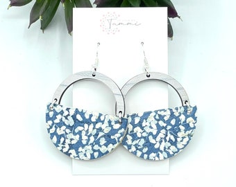 May include: A pair of blue and white floral patterned earrings with silver hoops. The earrings are made of wood and have a semi-circle shape.