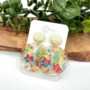 May include: Gold and clear resin earrings with a floral design and gold leaf accents. The earrings are round and have a textured gold top.