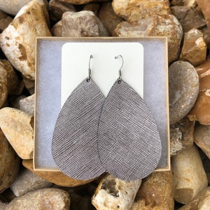 May include: A pair of silver teardrop-shaped leather earrings with a textured finish. The earrings have silver hooks.