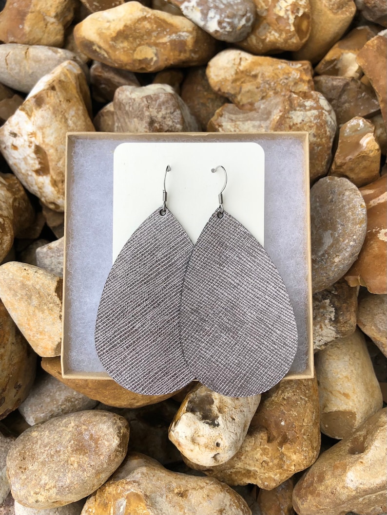 May include: A pair of silver teardrop-shaped leather earrings with a textured finish. The earrings have silver hooks.
