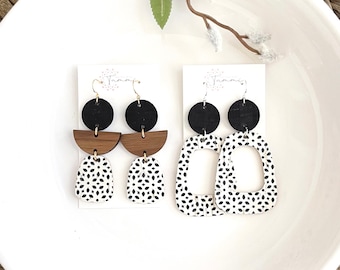 May include: Two pairs of geometric earrings. The first pair features black and brown circles with a white and black patterned teardrop shape. The second pair features a white and black patterned rectangle with a cutout.