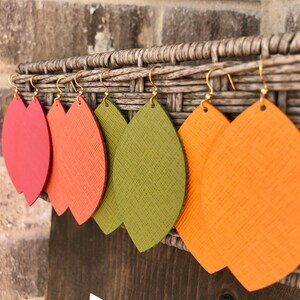 May include: Five pairs of leather earrings in the shape of leaves. The earrings are in shades of red, orange, and green.