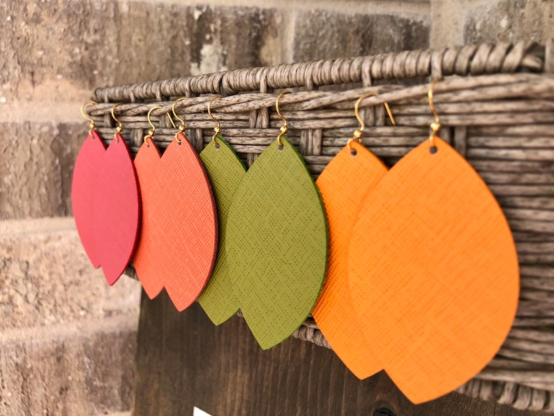 May include: Five pairs of leather earrings in the shape of leaves. The earrings are in shades of red, orange, and green.