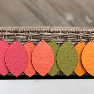 May include: Five pairs of leather earrings in a variety of fall colors. The earrings are shaped like teardrops and have a gold hook.
