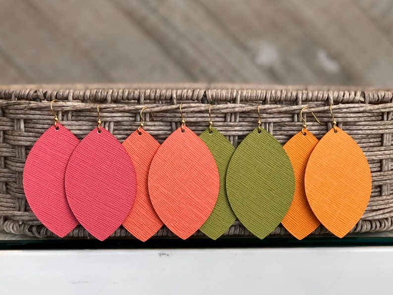 May include: Five pairs of leather earrings in a variety of fall colors. The earrings are shaped like teardrops and have a gold hook.