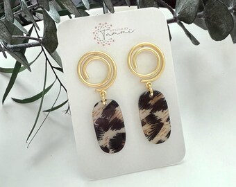 May include: Gold-coloured spiral earrings with oval pendants in a brown and cream animal print. The earrings are displayed on a white card with the text "DESIGN BY Tammi".