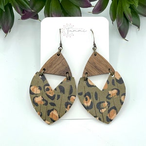 May include: A pair of green and brown leather earrings with a leopard print design. The earrings are shaped like a teardrop and have a wooden accent.