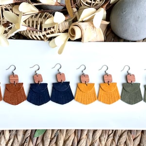 May include: A collection of seven handmade earrings in various colors, including brown, tan, navy, yellow, and olive green. Each earring features a small wooden square at the top and a fringed leather bottom, all with silver-tone hooks.