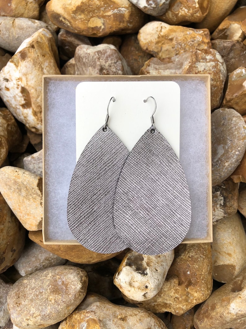 May include: A pair of silver teardrop-shaped leather earrings with silver hooks.