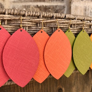 May include: Five pairs of dangle earrings with leaf-shaped leather pieces in shades of red, orange, and green. The earrings have gold-toned hooks.