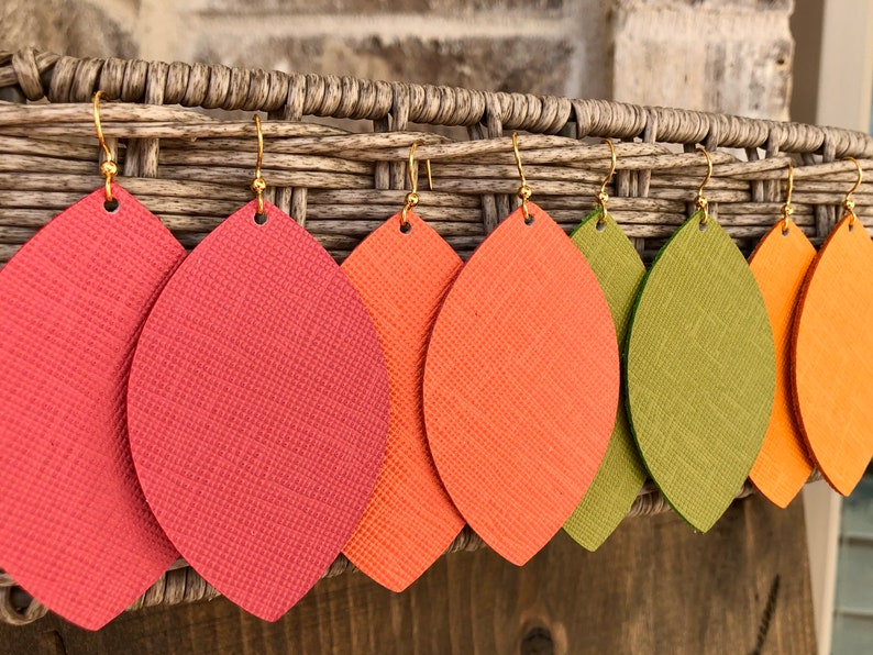 May include: Five pairs of dangle earrings with leaf-shaped leather pieces in shades of red, orange, and green. The earrings have gold-toned hooks.