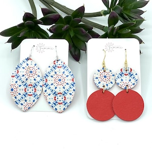 May include: Two pairs of earrings on white cards. The first pair is oval shaped with a blue and red patterned design. The second pair is a red circle with a smaller blue and red patterned circle on top.