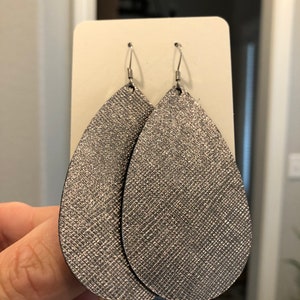 May include: A pair of silver teardrop-shaped earrings with a sparkly finish. The earrings are made of leather and have a silver hook closure.