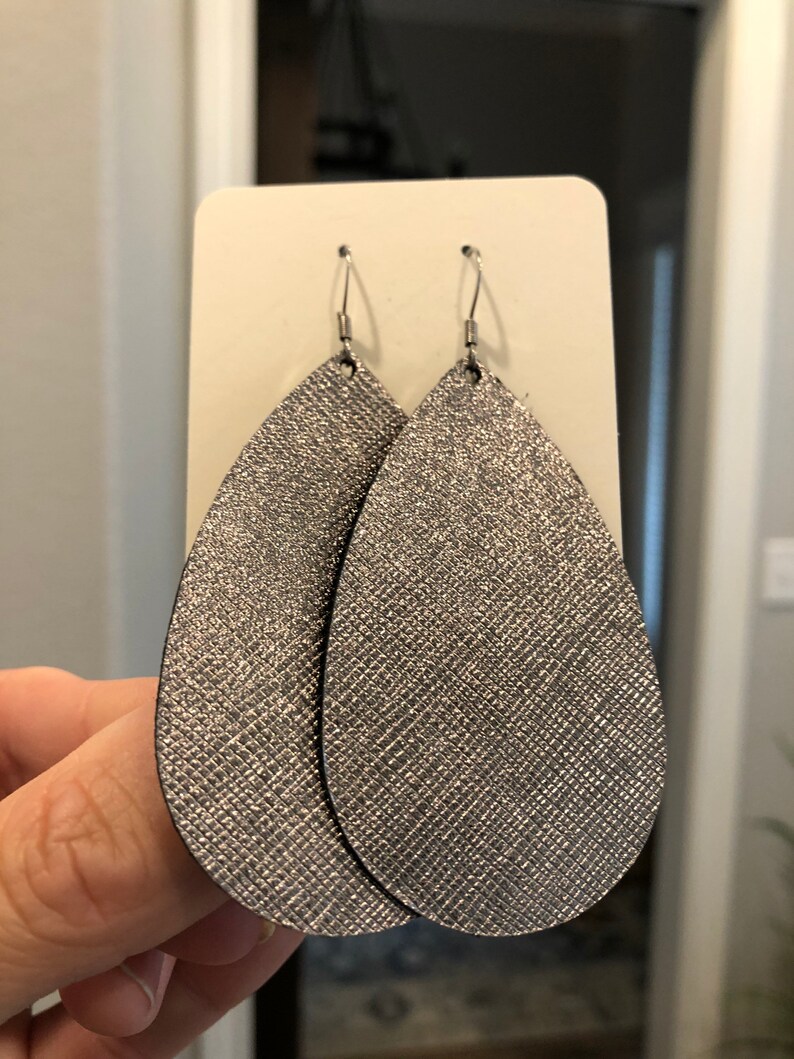 May include: A pair of silver teardrop-shaped earrings with a sparkly finish. The earrings are made of leather and have a silver hook closure.
