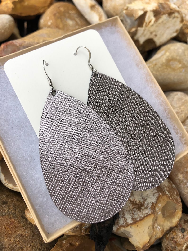 May include: A pair of silver teardrop-shaped earrings with a textured surface. The earrings are made of leather and have silver hooks.