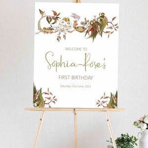 May include: A white sign with a green leafy border and the text "Welcome to Sophia-Rose's First Birthday Saturday 23rd June, 2023".