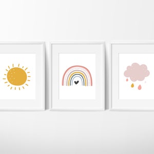 May include: Three framed prints with a minimalist design. The first print features a yellow sun with rays. The second print features a rainbow with a black heart in the center. The third print features a pink cloud with raindrops.