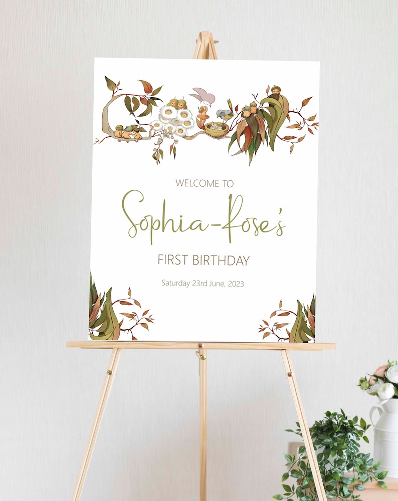 May include: A white sign with a green leafy border and the text "Welcome to Sophia-Rose's First Birthday Saturday 23rd June, 2023".