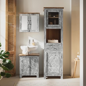 Könnte beinhalten: Ein Badezimmermöbel-Set mit weißem Used-Look und geschnitzten floralen Details. Das Set umfasst einen hohen Schrank, einen Waschtisch mit Waschbecken und einen Spiegelschrank. Das Holz hat eine natürliche braune Oberseite.