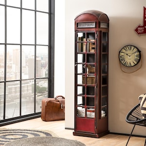 Könnte beinhalten: Ein hoher Schrank im Vintage-Stil, der einer britischen Telefonzelle nachempfunden ist. Der Schrank ist hauptsächlich dunkelrot mit einer Glastür und Regalen. Das Wort "TELEPHONE" ist oben aufgedruckt. Ein brauner Lederkoffer steht daneben.