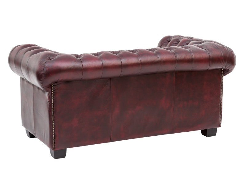 Op de afbeelding: Een bordeauxrode leren bank met gestoffeerde bekleding en een gerolde rugleuning. De bank heeft een klassiek ontwerp en is perfect voor een traditionele woonkamer.