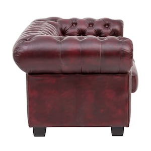 Op de afbeelding: Een bordeauxrode leren bank met een gestoffeerde rugleuning en gerolde armleuningen. De bank heeft een klassiek ontwerp en is perfect voor een traditionele woonkamer.