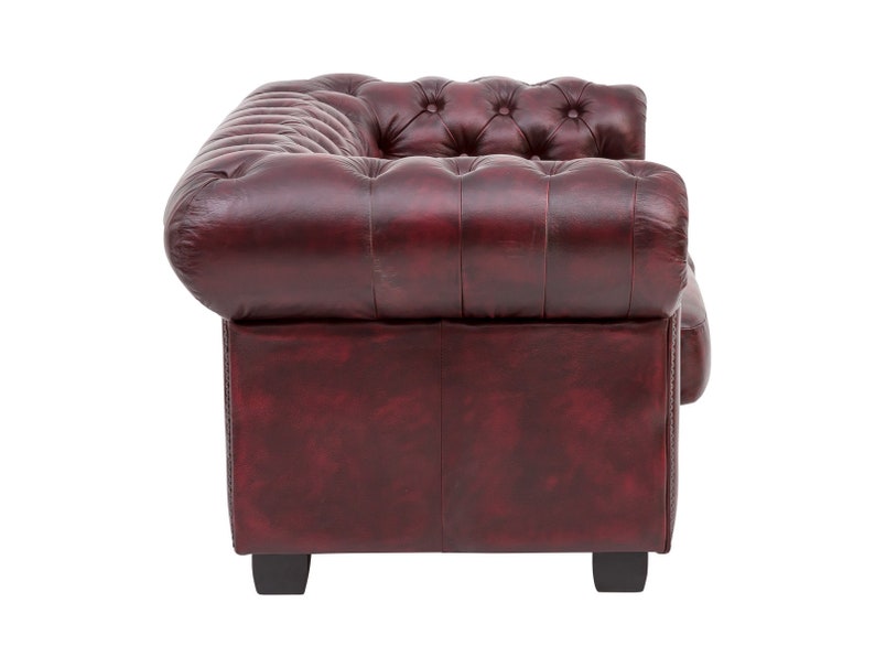 Op de afbeelding: Een bordeauxrode leren bank met een gestoffeerde rugleuning en gerolde armleuningen. De bank heeft een klassiek ontwerp en is perfect voor een traditionele woonkamer.