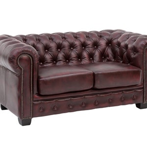 Op de afbeelding: Een bordeauxrode leren Chesterfield-bank met een klassiek ontwerp. De bank heeft een knoop-gecapitonneerde rugleuning en zitting, en gerolde armleuningen. De bank is gemaakt van hoogwaardig leer en heeft een stevig houten frame.