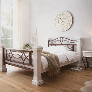 Könnte beinhalten: Ein weißes Bettgestell mit braunen Metallakzenten und dekorativen Pfosten. Das Bett ist mit weißer Bettwäsche und einer beigen Decke bezogen. Ein weißer Nachttisch mit Lampe und eine große Uhr sind im Hintergrund zu sehen.