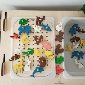 May include: Wooden animal puzzle with colorful animal shapes, including a giraffe, dolphin, and bear. The puzzle pieces are designed to fit into a wooden board with a white border. The image also shows a tray with additional puzzle pieces.