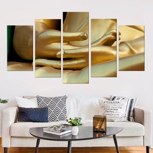 Puede incluir: Un conjunto de cinco impresiones en lienzo que presenta un primer plano de las manos de una estatua dorada de Buda en una pose meditativa.