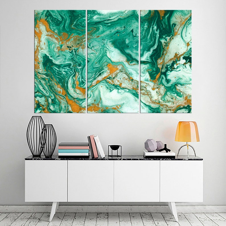 May include: A three-piece abstract art print set featuring a swirling green and gold marble pattern. The print is displayed on a white wall above a white cabinet with black legs.