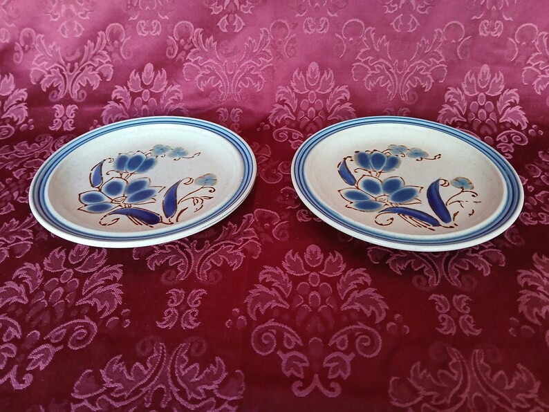 K&ouml;nnte beinhalten: Zwei ovale Keramikplatten mit blauem Blumendesign. Die Teller haben eine cremefarbene Mitte mit blauen Blumenmustern und einen blau-braunen Rand. Diese Teller dienen wahrscheinlich zum Servieren von Speisen.